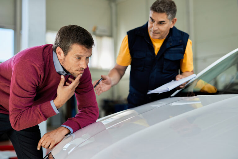 uncertain man examining his car hood while mechanic is talking his auto repair shop scaled